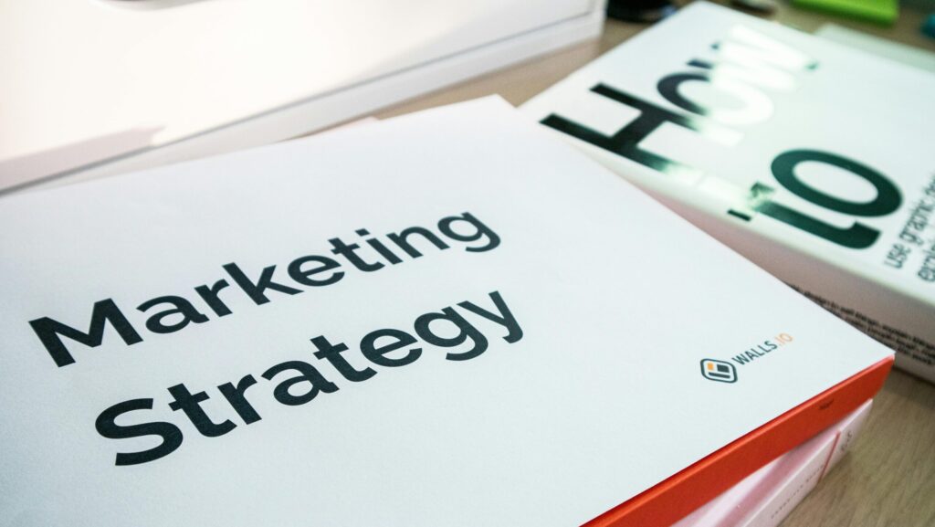 A printed "Marketing Strategy" booklet resting on a stack of books on a desk.